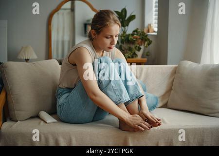 Entspannte Frau, die auf dem Sofa sitzt und die Zehennägel untersucht Stockfoto