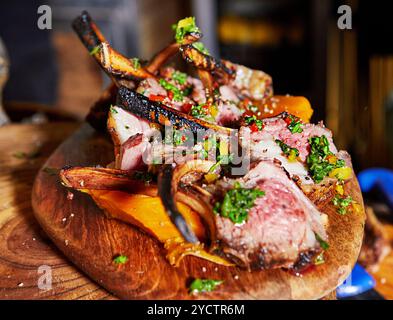 Perfekt gegrillte Lammkoteletts auf einem Holzbrett, begleitet von frischem Gemüse und garniert mit Kräutern, servierfertig. Stockfoto