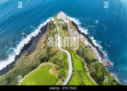 Aus der Vogelperspektive einer kurvigen Straße, die zu einem Leuchtturm auf den Azoren führt (Farol da Ponta do Arnel ) Stockfoto