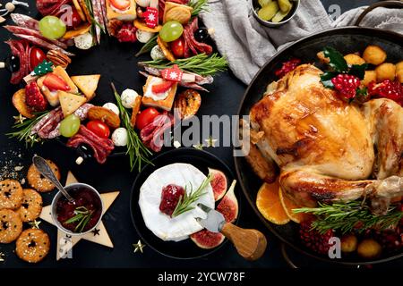 Konzept des Weihnachts- oder Neujahrsessens mit gebratenem Huhn und verschiedenen Vorspeisen auf dunklem Hintergrund. Draufsicht. Stockfoto