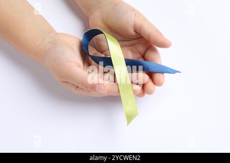 Kind mit gelbem und blauem Band auf weißem Hintergrund, Nahaufnahme. Down-Syndrom-Bewusstsein Stockfoto