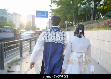 Ein Paar in traditioneller Kleidung läuft die Straße hinunter. Der Mann trägt eine blaue Jacke und die Frau ein weißes Kleid Stockfoto