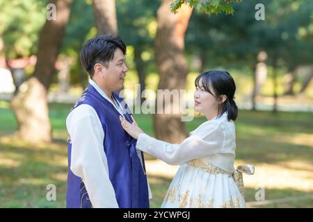 Mann und Frau stehen in einem Park. Der Mann trägt eine blaue Jacke und die Frau ein weißes Kleid Stockfoto