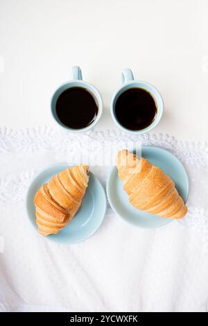 Zwei Tassen Kaffee und Croissants auf dem Hintergrund der Schnürsenkel auf einem weißen Hintergrund, Nahaufnahme Stockfoto