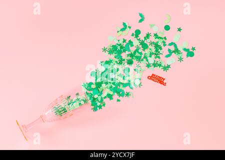 Weihnachtskomposition mit grünem und rotem Glitzerkonfetti und rosa Sektglas auf pastellrosa Hintergrund. Festliche Weihnachtskulisse in Pastellfarben. Stockfoto