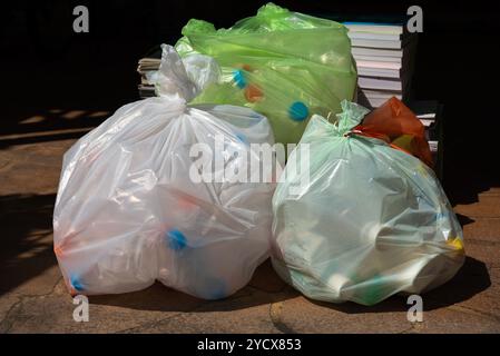 Nahaufnahme mehrerer Plastikbeutel, gefüllt mit verschiedenen recycelbaren Materialien, einschließlich Flaschen und Behältern, auf einer Außenfläche. Stockfoto