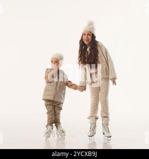 Lachend und verspielt, umarmen sich Geschwister während ihrer weihnachtlichen Eislaufsession vor weißem Studio-Hintergrund. Stockfoto