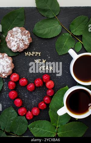 Neujahrsinschrift auf einem schwarzen Brett mit Cupcake und Herz in Form von Kirschen Stockfoto