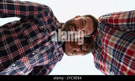 Blick aus dem niedrigen Winkel von jungen Männern, Zwillingen, gekleideten Casual, passenden Outfits, die auf die Kamera vor weißem Studiohintergrund schauen. Collage. Gemütliches Selfie Stockfoto