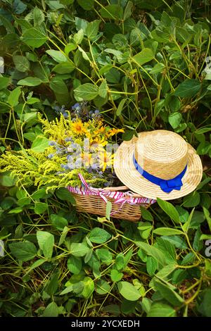 Strohhut und Korb mit Blumen stehen auf dem Gras Stockfoto