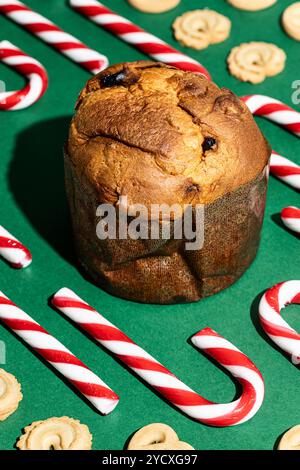 Blick von oben auf ein traditionelles Weihnachtspanettone, umgeben von Zuckerstangen und Butterkeksen auf einem lebhaften grünen Hintergrund, das Weihnachtssüße feiert Stockfoto