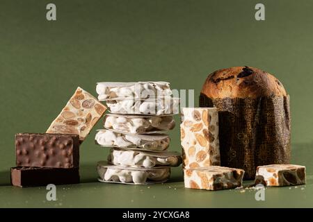 Verschiedene Weihnachtsbonbons, die elegant auf grünem Hintergrund angeordnet sind. Die Auswahl umfasst Schokoladentafeln, Stapel von Puffreis-Nougat, Bonbons und Stockfoto