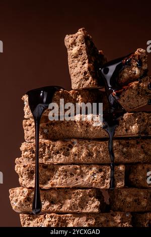 Nahaufnahme von aufgeschnittener Schokolade und aufgebautem Reisnougat, zusammengestapelt und mit Sirup getränkt, auf dunklem Hintergrund. Dieses verführerische Leckerli verleiht Ihrem Look Glanz Stockfoto