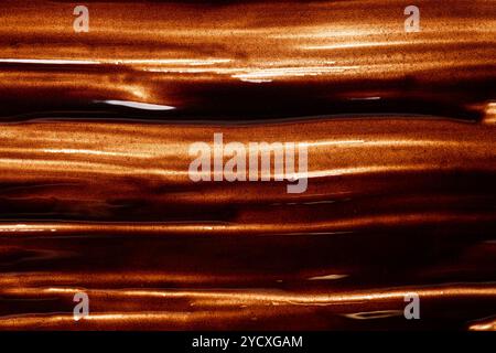 Nahaufnahme einer glänzenden, geschmolzenen Schokoladenoberfläche mit welligen Wellen, die Licht reflektieren und eine luxuriöse und samtige Textur suggerieren. Stockfoto