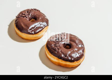 Zwei vegane Donuts mit einer reichhaltigen, glänzenden Schokoladenglasur und zarten Schokoraspeln bieten diese süßigkeiten auf pflanzlicher Basis eine perfekte Balance aus swee Stockfoto