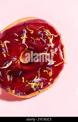 Exquisites Stockbild eines veganen Donuts mit leuchtenden roten Früchten, der mit essbaren Blumen geschmückt ist und eine verlockende und künstlerische Präsentation auf einem Pas zeigt Stockfoto