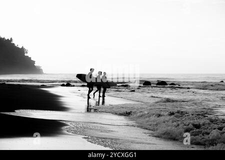 Die Silhouette unbekannter Surfer trägt ihre Boards an einem Strand in El Salvador, der sich vor der untergehenden Sonne über dem Pazifik befindet. Die sce Stockfoto