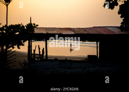 Nicht erkennbare Silhouette einer Person, die bei einem wunderschönen Sonnenuntergang in El Salvador, Zentralamerika, alleine an einem ruhigen Strand spaziert. Die friedliche Szene ist Stockfoto