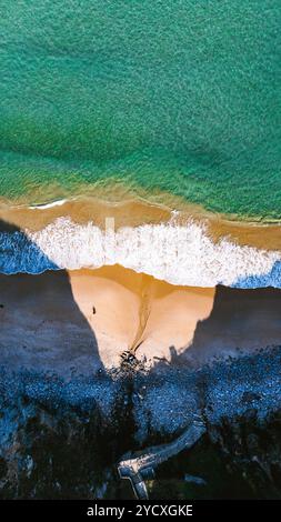 Atemberaubende Drohnenaufnahme, die einen wunderschönen Strand in Galicien erfasst und den lebhaften Kontrast zwischen dem azurblauen Wasser, dem sandigen Ufer und dem üppigen Grün unterstreicht Stockfoto