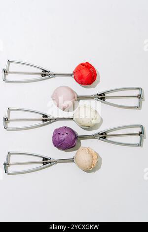 Fünf Eislöffel aus Metall, jeder mit einem unterschiedlich schmeckenden Löffel aus Rot, Rosa, weiß, Blau und Beige auf einem schlichten weißen Hintergrund. Stockfoto