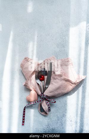 Eine elegante Tischeinrichtung mit einer weichen rosa Serviette, Besteck aus Edelstahl, einer roten Herzdekoration und einem Band mit Herzmotiven ist perfekt Stockfoto
