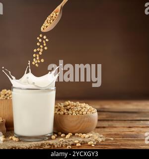 Sojabohnen fallen vom Löffel in ein Glas Pflanzenmilch auf Holztisch. Leerzeichen für Text Stockfoto