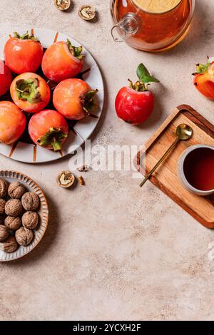 Eine einladende Herbstspeise mit saftigen Persimmonen auf einem Teller, neben einer Schüssel mit Walnüssen und einer Kanne mit frischem Saft auf einer rustikalen Steinoberfläche Stockfoto