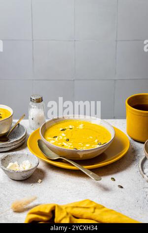 Cremige Kürbissuppe mit Kürbiskernen und zerbröckeltem Feta, serviert in handwerklicher Keramik vor grauem Hintergrund dieses saisonale Gericht verkörpert den Autu Stockfoto