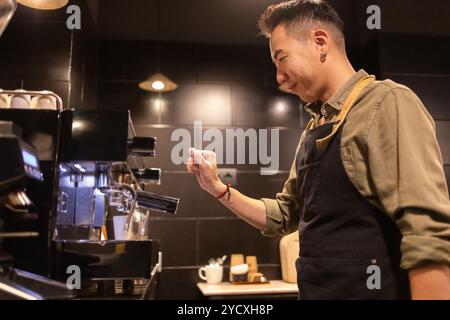 Ein erfahrener asiatischer Barista bedient aufmerksam eine hochwertige Espressomaschine in einem eleganten, modernen Café-Ambiente und konzentriert sich auf die Zubereitung der perfekten Tasse Stockfoto