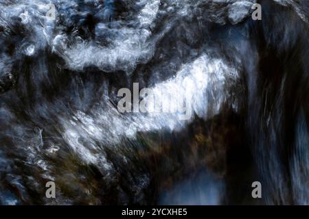 Eine Nahaufnahme, die die dynamische und abstrakte Bewegung des Wassers einfängt, das über Felsen fließt und eine verschwommene, fließende Textur aufweist. Stockfoto