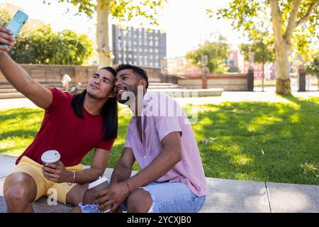 Ein liebevolles schwules Paar lateinamerikanischer und afroamerikanischer Abstammung macht ein Selfie in einem Stadtpark, in dem sie einen freudigen Moment teilen und die Lebendigkeit von zeigen Stockfoto