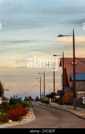 Ein ruhiger Blick auf den Mont Blanc vom Col de la Faucille im französischen Jura, in der Abenddämmerung mit Silhouetten von Straßenlaternen und alpinen Häusern Lini erfasst Stockfoto