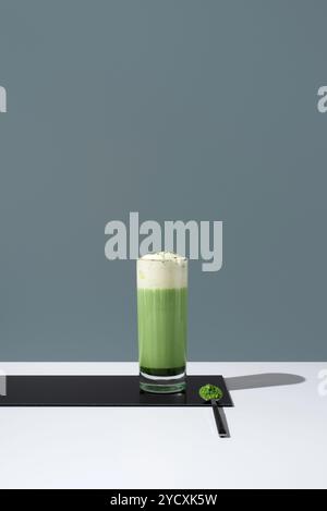 Ein großes Glas leuchtenden grünen Matcha-Tee mit luftiger Schlagsahne steht auf einer eleganten Oberfläche und strahlt minimalistische Eleganz und erfrischende Vibes aus. Stockfoto