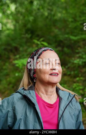 Eine reife Frau mit einem hellen Lächeln läuft durch einen grünen Wald und zeigt Vitalität und einen positiven Lebensstil in ihren goldenen Jahren Stockfoto