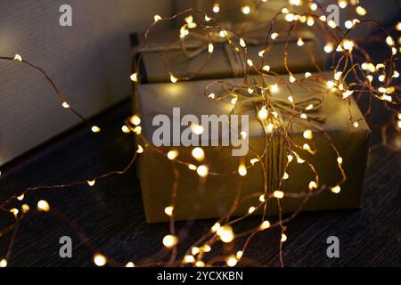 Ein wunderschön gewickeltes Weihnachtsgeschenk aus goldenem Papier, verschlungen mit glitzernden Lichterketten, die ein warmes, festliches Leuchten verleihen, perfekt für saisonale Backgr-Fans Stockfoto