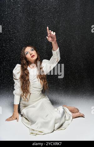 Eine junge Frau, elegant gekleidet mit weißen Gesten nach oben, glitzernde Tropfen umgeben sie. Stockfoto