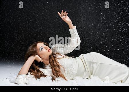 Eine junge Frau lehnt sich elegant zurück, fasziniert von Schneeflocken, die um sie herum herumtreiben. Stockfoto