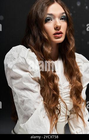 Die junge Frau mit fließenden Haaren präsentiert sich in einer schicken weißen Bluse mit einem fesselnden Look. Stockfoto