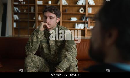 Verärgert depressive Verzweiflung kaukasischer männlicher Militärsoldat Veteran Tarnung Uniformoffizier mit Schmerz Kopf halten denken drinnen mit sitzen Stockfoto