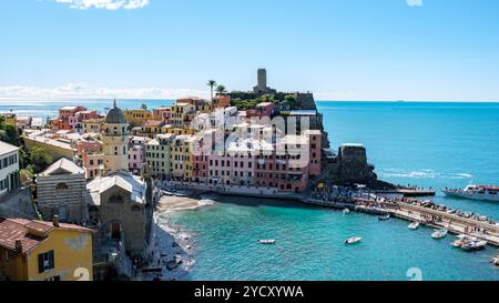 Eingebettet zwischen azurblauem Wasser und zerklüfteten Klippen glitzern die farbenfrohen Häuser von Vernazza Cinque Terre unter einem hellen Himmel und laden Reisende ein, den Charme und das reiche Erbe Italiens zu erkunden Stockfoto