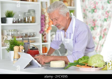 Älterer Mann in der Schürze, der zu Hause gesunde Nahrung zubereitet Stockfoto