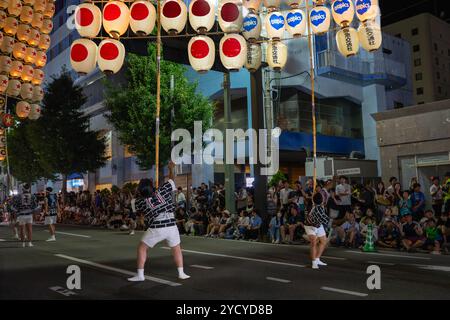 Akita City, Japan – 5. August 2024: Künstler balancieren hohe Bambusstangen mit mehreren Laternen an verschiedenen Körperteilen und zeigen ihre Fähigkeiten auf der Stockfoto