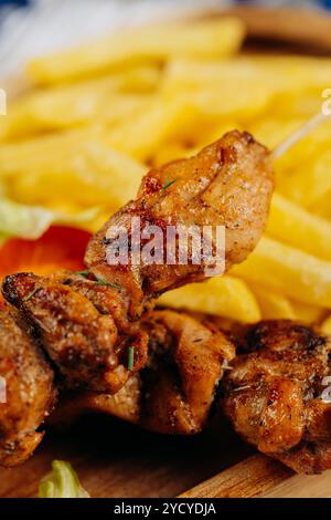 Nahaufnahme saftiger gegrillter Hähnchenspieße mit knusprigen Pommes Frites, perfekt zum Mittag- oder Abendessen Stockfoto