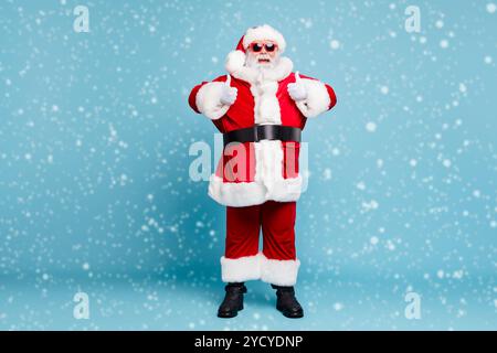 Volle Länge Körper Größe seiner Er schönen kühlen Heiter froh Fetten bärtigen Santa tragen warmen Wintermantel schauen Outfit mit zwei Doppel thumbup Stockfoto