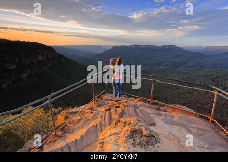 Eine Frau fängt mit ihrem Handy einen atemberaubenden Sonnenaufgang über bergige Landschaft ein Stockfoto