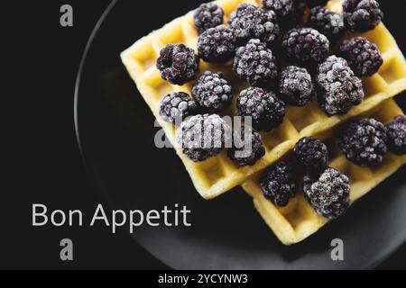 Belgische Waffeln mit Gefrorene Brombeeren auf schwarzem Hintergrund, Inschrift bon appetit Stockfoto