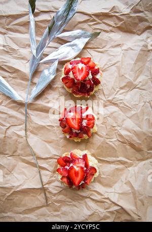 Schöne kleine Kuchen mit Erdbeeren zusammen mit einem Zweig auf Kraftpapier Stockfoto