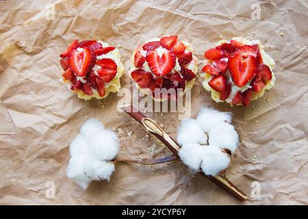 Schöne kleine Kuchen mit Erdbeeren zusammen mit einem Zweig der Baumwolle liegt auf Kraftpapier Stockfoto