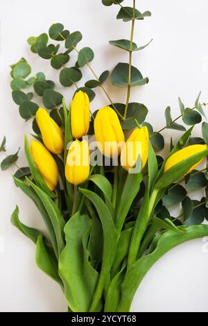 Schöne gelbe Tulpen mit Eukalyptuszweigen auf einem weißen Tisch Stockfoto