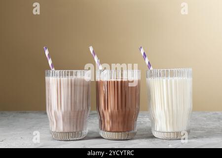 Köstliche Proteinshakes in Gläsern auf grauem, strukturiertem Tisch vor beigefarbenem Hintergrund Stockfoto